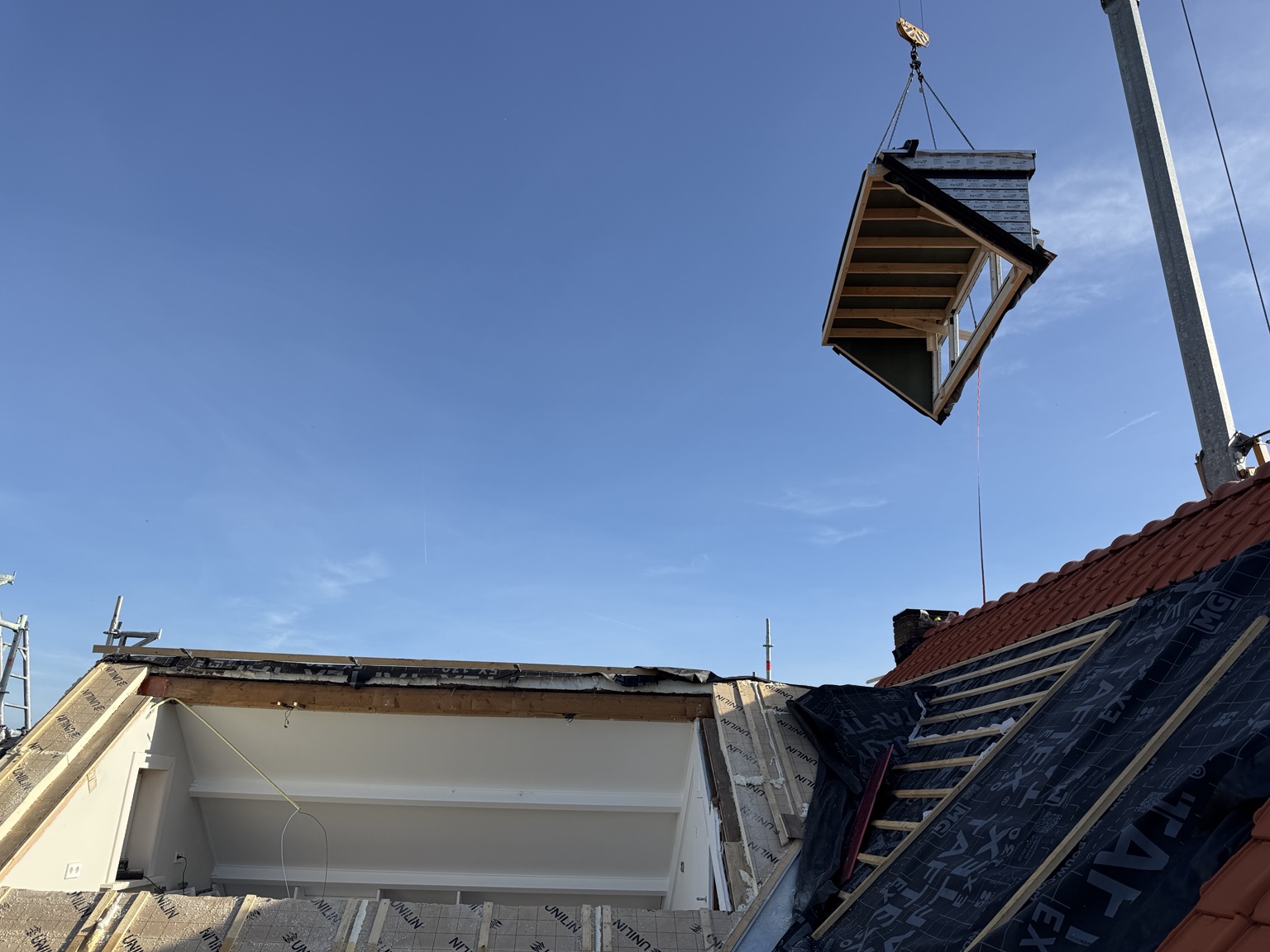 Prefab dakkapel wordt met een kraan boven het dak gehesen